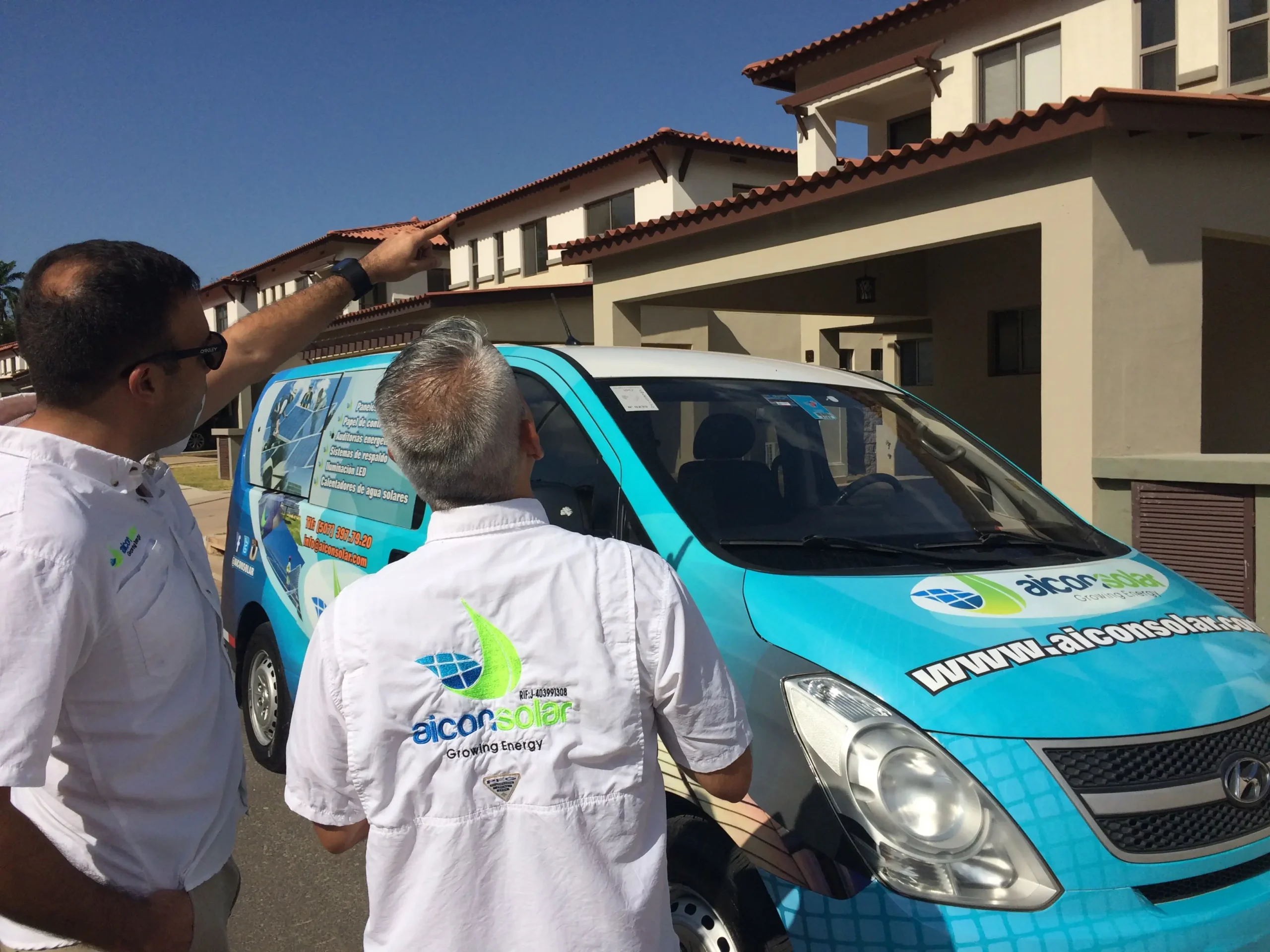 Two Aicon Solar staff discussing a rooftop project beside branded van.