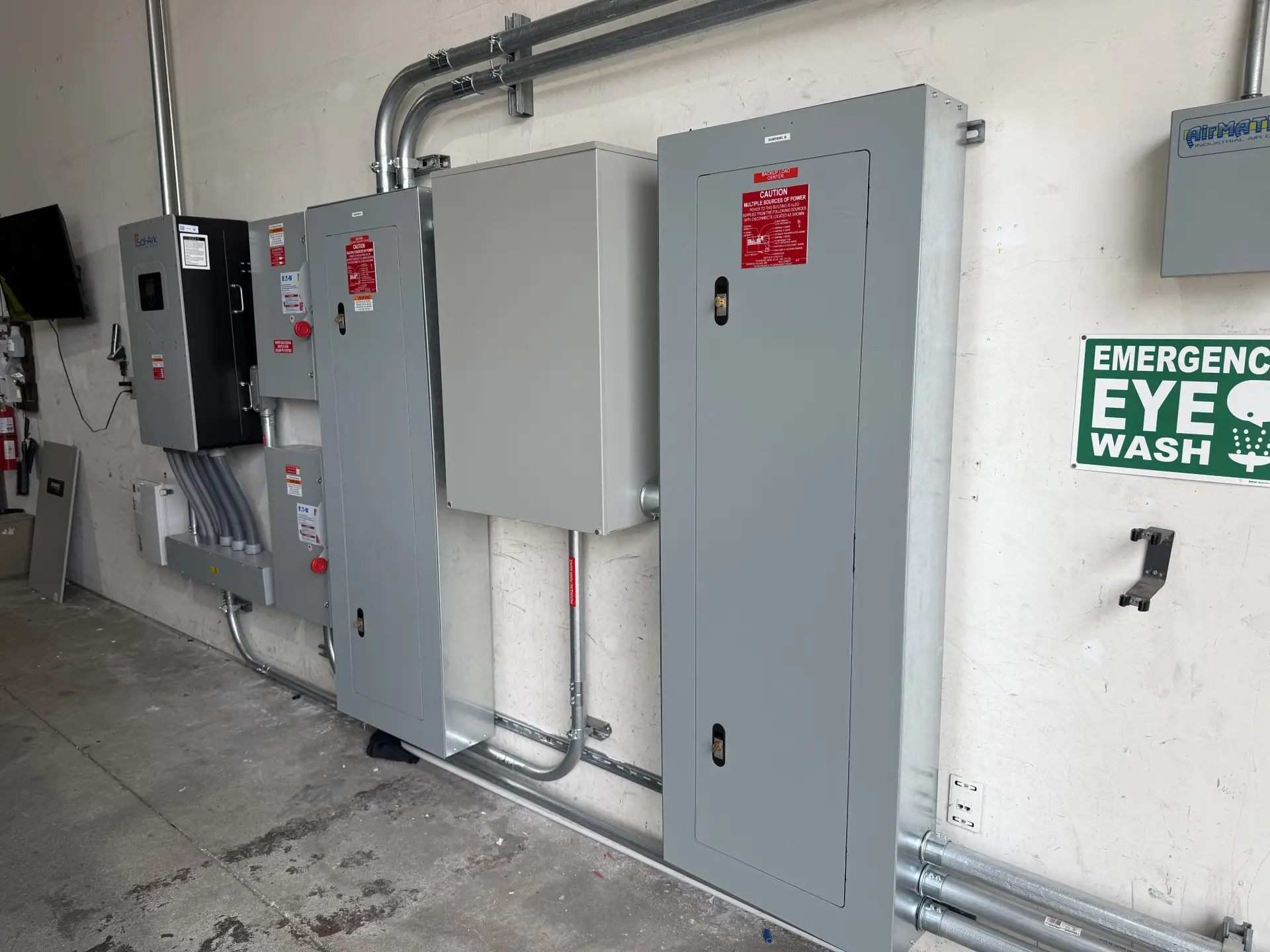 Electrical control panels and inverters mounted on concrete interior wall.