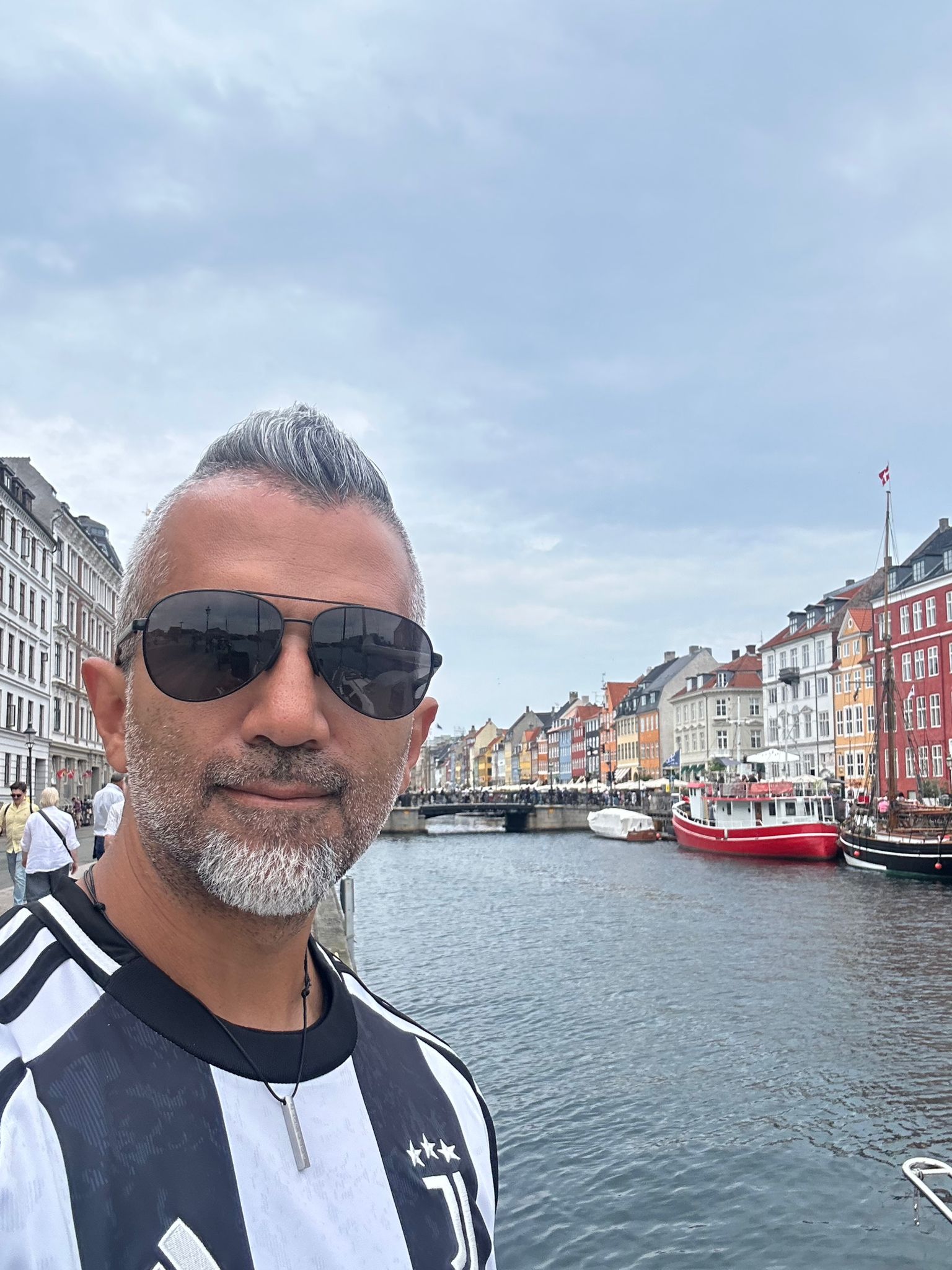 Man with sunglasses at a colorful canal-side cityscape, likely in Europe.