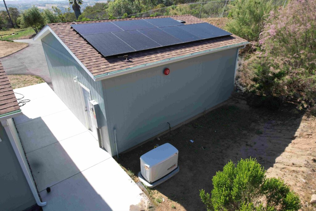 Small building with solar panels on roof and generator on ground.