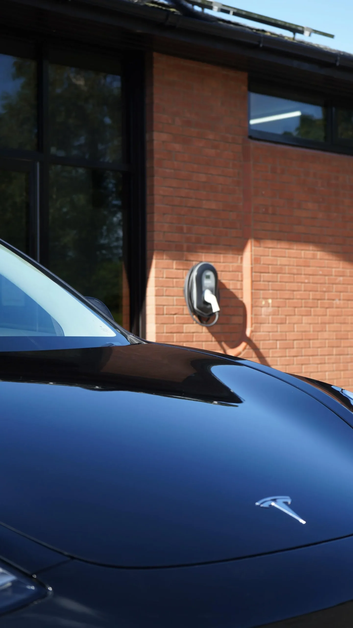 Tesla parked outside near wall-mounted home charging unit.