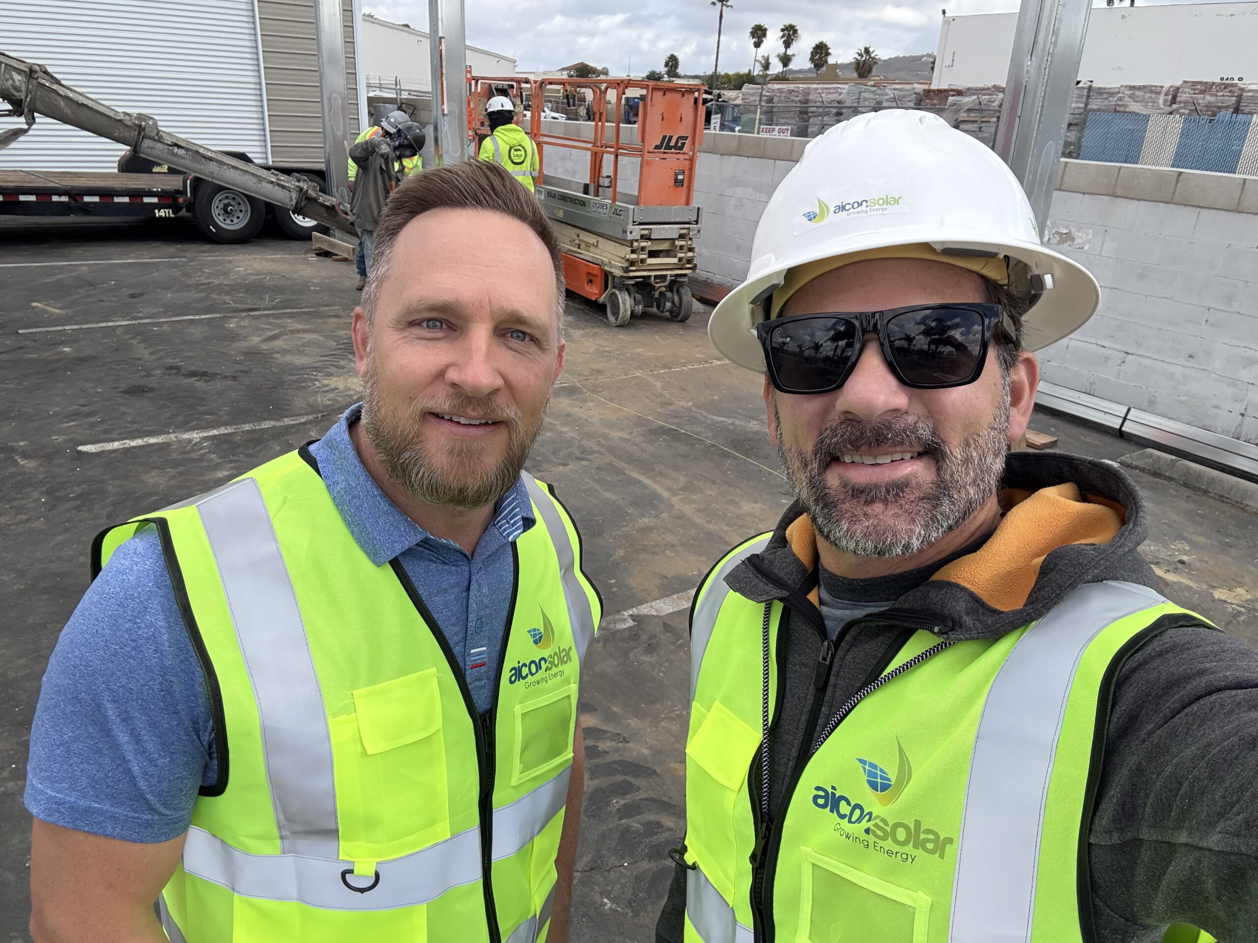 Two Aicon Solar team members on construction site wearing safety vests.