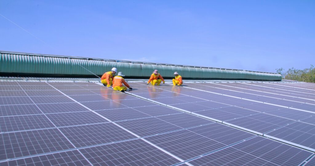 Workers in yellow suits installing large solar panels on rooftop.