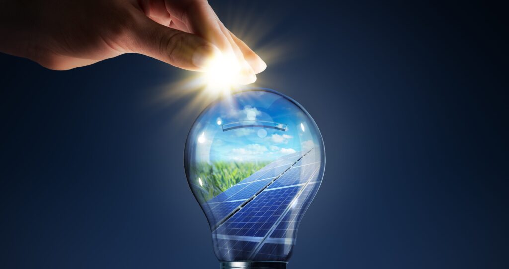 Hand lighting up a bulb with solar panel reflection inside.
