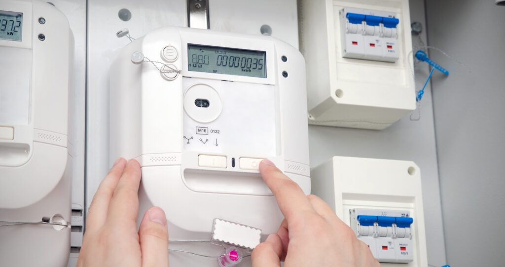 Hands pressing buttons on a digital electricity meter on a control panel.