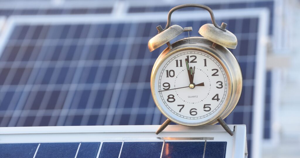 Vintage alarm clock on top of solar panels in morning sunlight.